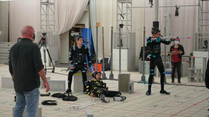 Miles Robbins, Evan Evagora e Justice Smith atuam em trajes de captura de performance no set de uma cena do jogo The Quarry.