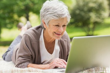 Улыбающаяся старшая женщина, использующая ноутбук в парке