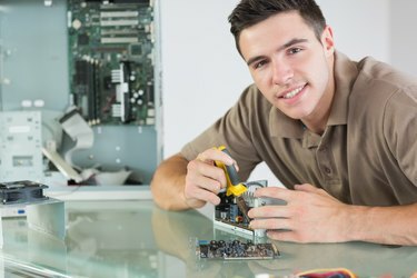 Przystojny uśmiechnięty inżynier komputerowy naprawiający sprzęt za pomocą szczypiec