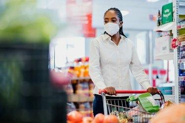 Kobieta robi zakupy w supermarkecie, nosząc maskę na twarz z koronawirusem.