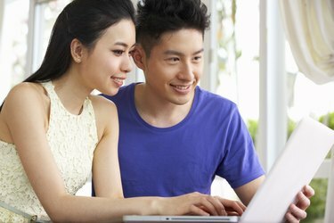 Tânăr cuplu chinez așezat la birou și folosind laptopul acasă
