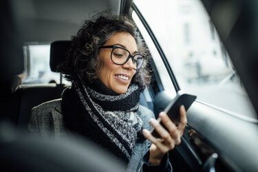 Moden forretningskvinde bruger telefon, mens hun rejser med en taxa