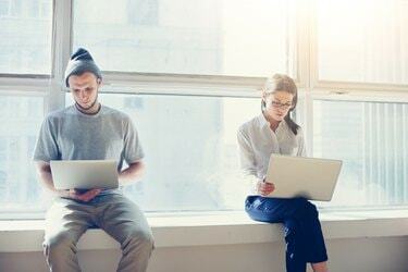 Homem e mulher com laptops perto de uma grande janela brilhante