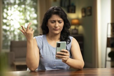 Mujer joven india que usa el teléfono en casa, foto común