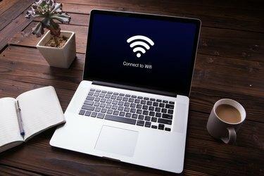Wi-Fi ryšio vaizdas nešiojamojo kompiuterio ekrane su biuro įranga medinio stalo fone