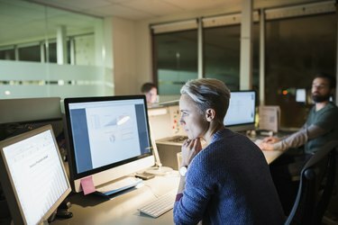 Forretningskvinne jobber sent ved datamaskiner på kontoret