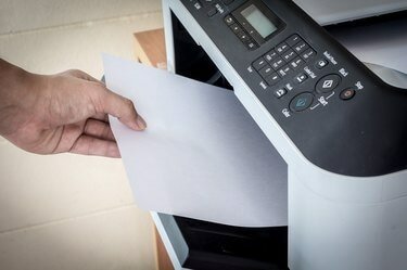 Mão segurando as folhas de papel na bandeja da impressora