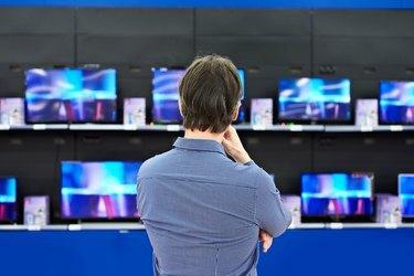 Un bărbat se uită la televizoarele LCD din magazin