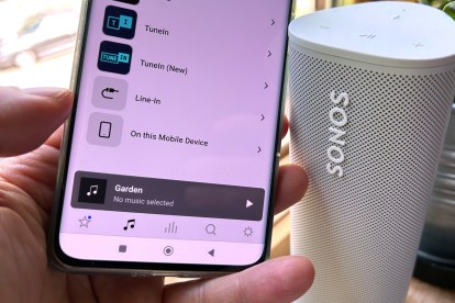 Ένα τηλέφωνο Android με την εφαρμογή Sonos που εμφανίζει το μενού της καρτέλας πηγές μουσικής, δίπλα σε ένα ασύρματο ηχείο Sonos Roam.