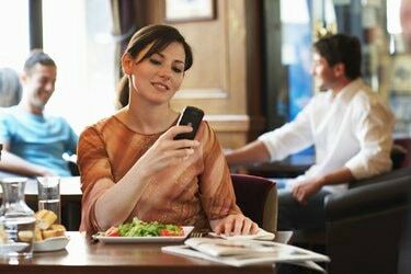 Vrouw zittend aan tafel in bar, kijkend naar mobiele telefoon, glimlachend