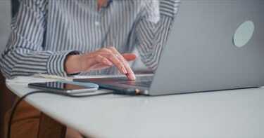 Nahaufnahmehand der jungen schönen Geschäftsfrau, die mit Laptop-Touch-Bar am hellen modernen minimalistischen Bürotisch arbeitet.