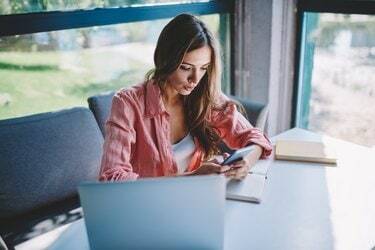 流行に敏感な女性ブロガーは、カフェのコンピューターに座っている4Gインターネットを使用して最新のスマートフォンで通知付きの電子メールをチェックしています。 コーヒーショップの電話デバイスでオンラインチャットするミレニアル世代の若い女性