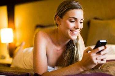 Mulher enviando mensagens de texto em um telefone celular em um quarto de hotel, Papeete, Taiti, Polinésia Francesa