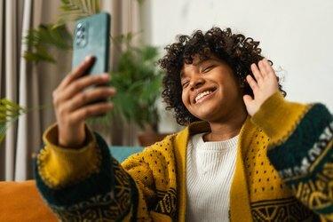 Afroamerikansk pige, der holder smartphone og har videochat. Kvindelig blogger chatter med bedste venner i sociale netværk. Ung kvinde har virtuelt møde online chat videoopkald derhjemme.