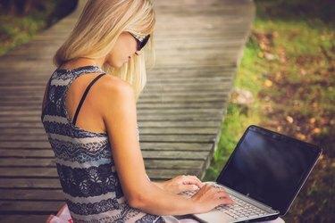 Młoda, piękna kobieta odpoczywa w parku i korzysta z laptopa.