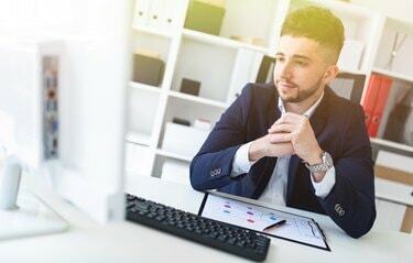 Um jovem sentado no escritório em uma mesa de computador e trabalhando com documentos.