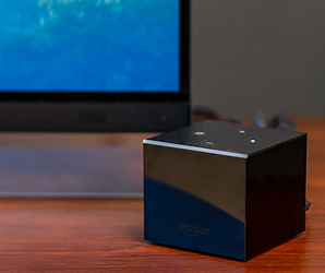 Amazon Fire TV Cube på ett bord med en TV i bakgrunden. 