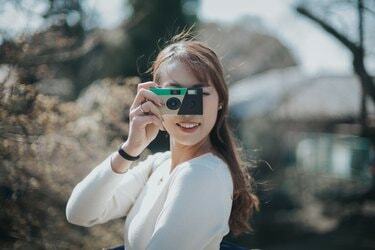 Радісна молода жінка фотографує з одноразовою камерою в парку в чудовий сонячний день
