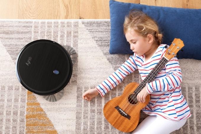 眠っている子供の隣のカーペットの上にある Eufy BoostIQ RoboVac 11S。