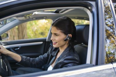 Vrouw in auto met oortelefoon van mobiele telefoon