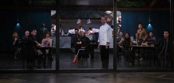 El chef y los invitados de un restaurante se giran y miran por la ventana en una escena de The Menu.