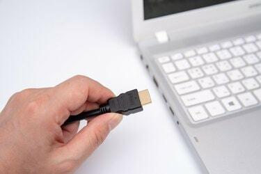 Un bărbat conectează cablul HDMI negru la laptop.