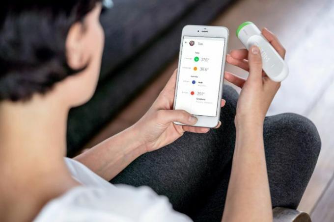Withings - Thermo Smart Temporal Thermometer се сравнява с цифровия дисплей от човек, изглед през рамото.