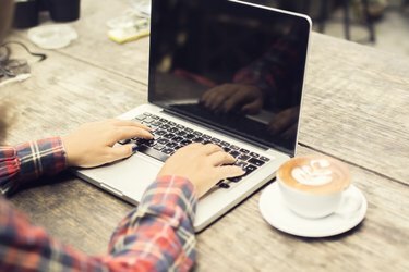 אישה מקלידת על מחשב נייד עם כוס קפה