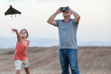 Fotografia otca, ktorý sleduje, ako jeho dcéra vypúšťa do vzduchu PowerUp FPV Paper Airplane VR Drone.