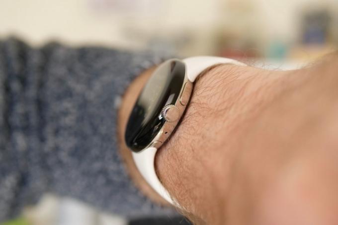 „Google Pixel Watch“ šoninis vaizdas ir karūnėlė, nešiojama ant vyro riešo.