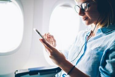 Млада жена меломан слуша любими песни по време на полет в кабина първа класа, използвайки мобилен плейлист и аксесоар, жена се забавлява на борда на самолета и се наслаждава на музика в слушалки от смартфон