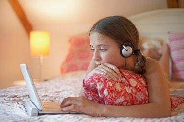 Девочка-подросток, лежа на кровати с помощью ноутбука