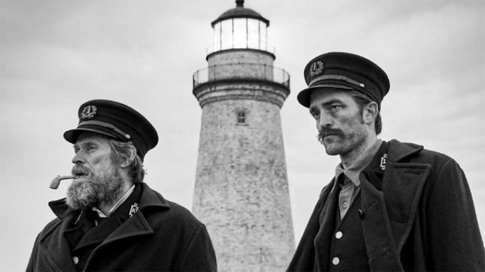 Willem Dafoe och Robert Pattinson i karaktär med en fyr i bakgrunden i The Lighthouse. 
