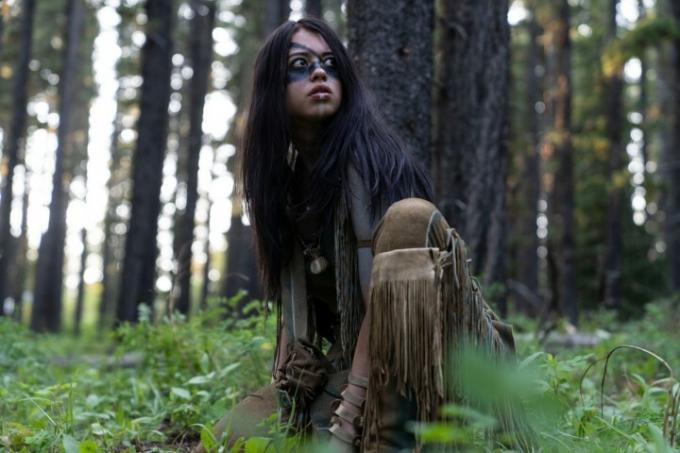 Amber Midthunder hukar sig i skogen och ser sig omkring i en scen från Prey.