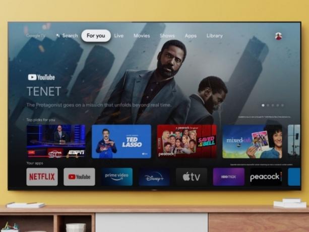 Açık kahverengi bir duvara monte edilmiş, ana ekran uygulamalarını gösteren Sony 77 inç Bravia TV