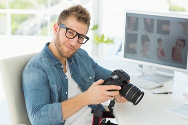 Knappe fotograaf die zijn camera vasthoudt terwijl hij naar de camera lacht