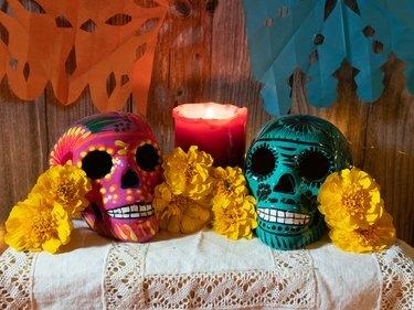 Kompozicija tradicionalnega oltarja za mehiški dan mrtvih z lobanjo, svečami, daritvijo in rožami.