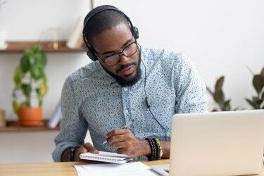Фокусиран африкански бизнесмен в слушалки, който пише бележки, гледайки уебинар