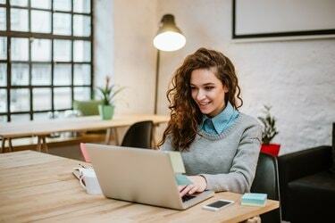 Succesvolle jonge vrouw in modern kantoor dat op laptop werkt.