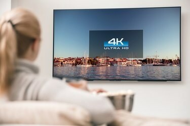 Liels, mūsdienīgs televizors ar 4K izšķirtspēju un jauna sieviete, kas skatās video