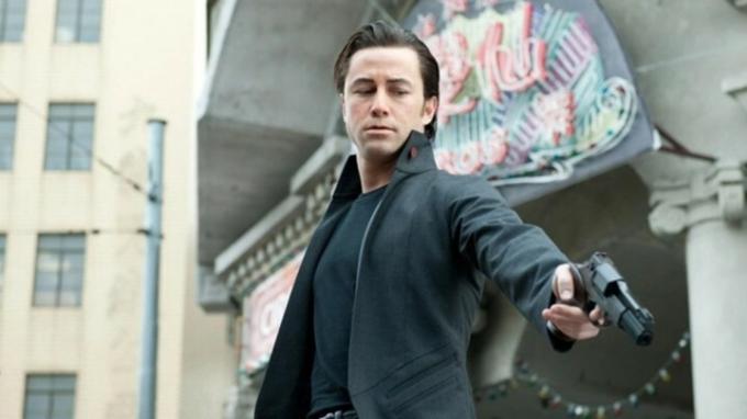 Un homme pointe son arme vers le sol dans Looper.