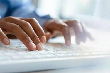 Händerna på den unga kvinnan som skriver på datorns tangentbord
