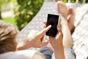 Muž používa mobilný chytrý telefón pri relaxácii v hojdacej sieti