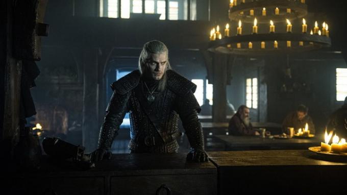 Geralt avec ses mains sur une table à l'air sérieux dans The Witcher.