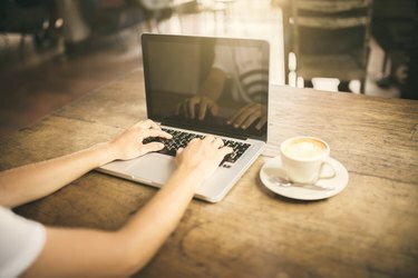 Flicka som skriver på ett tangentbord för bärbar dator på ett café