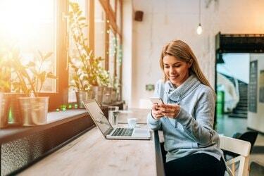 Kvinna som använder smartphone och bärbar dator på ett härligt ljust kafé.