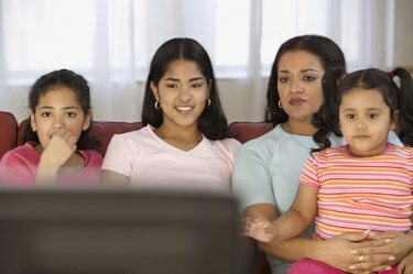 Femeie adultă mijlocie care se uită la televizor cu cele trei fiice ale ei