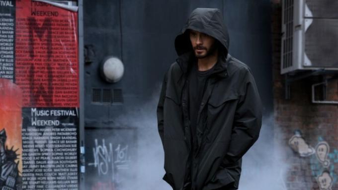 Jared Leto hodi v dežnem plašču s kapuco v prizoru iz Morbiusa.