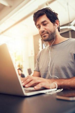 Homem caucasiano sentado em uma cafeteria usando um laptop