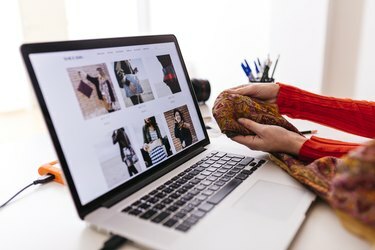 Крупни план модног дизајнера у студију са лаптопом који испитује тканину